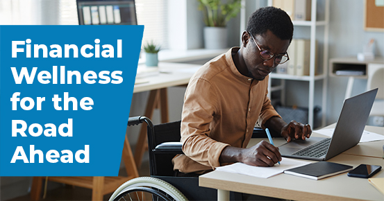 A person sitting on a desk, taking notes and using the computer.