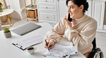 A person sitting on a desk, speaking on the phone and taking notes.