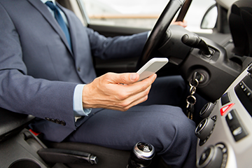 Hand holding a mobile device while businessman in car texts and drives behind the wheel