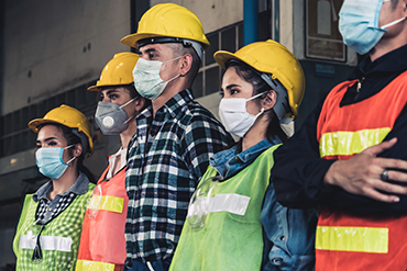 A group of five warehouse workers standing sholder to sholder and wearing face masks