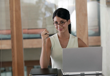 Woman wearing glasses and smiling at camera while sitting behind a laptop computer