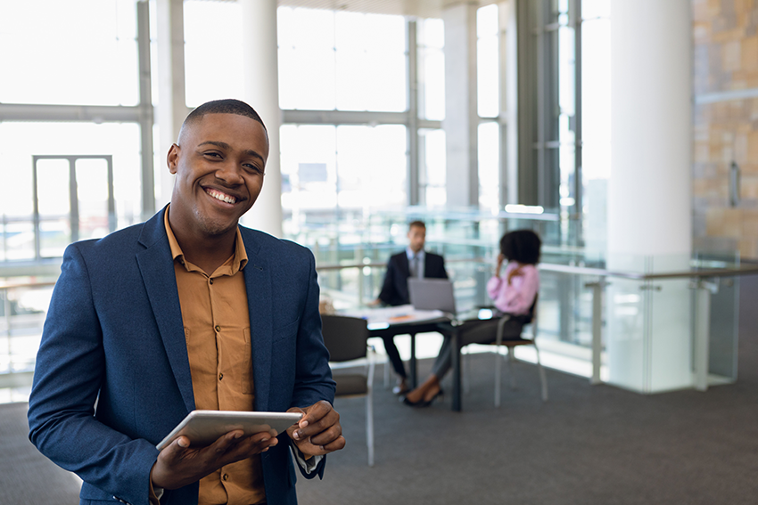 Smiling African American businessman in foreground holding a tablet computer with clients in the background 