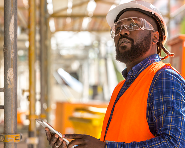 African American construction supervisor surveying his jobsite with a tablet computer in hand