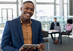 Smiling African American businessman in foreground holding a tablet computer with clients in the background 