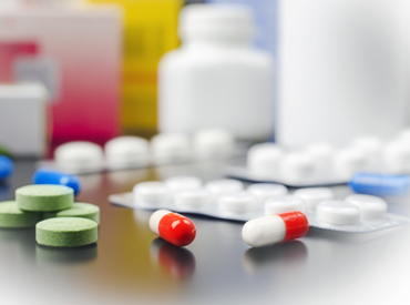 Photo of different colored prescription pills on a table with white prescription bottles in the background.