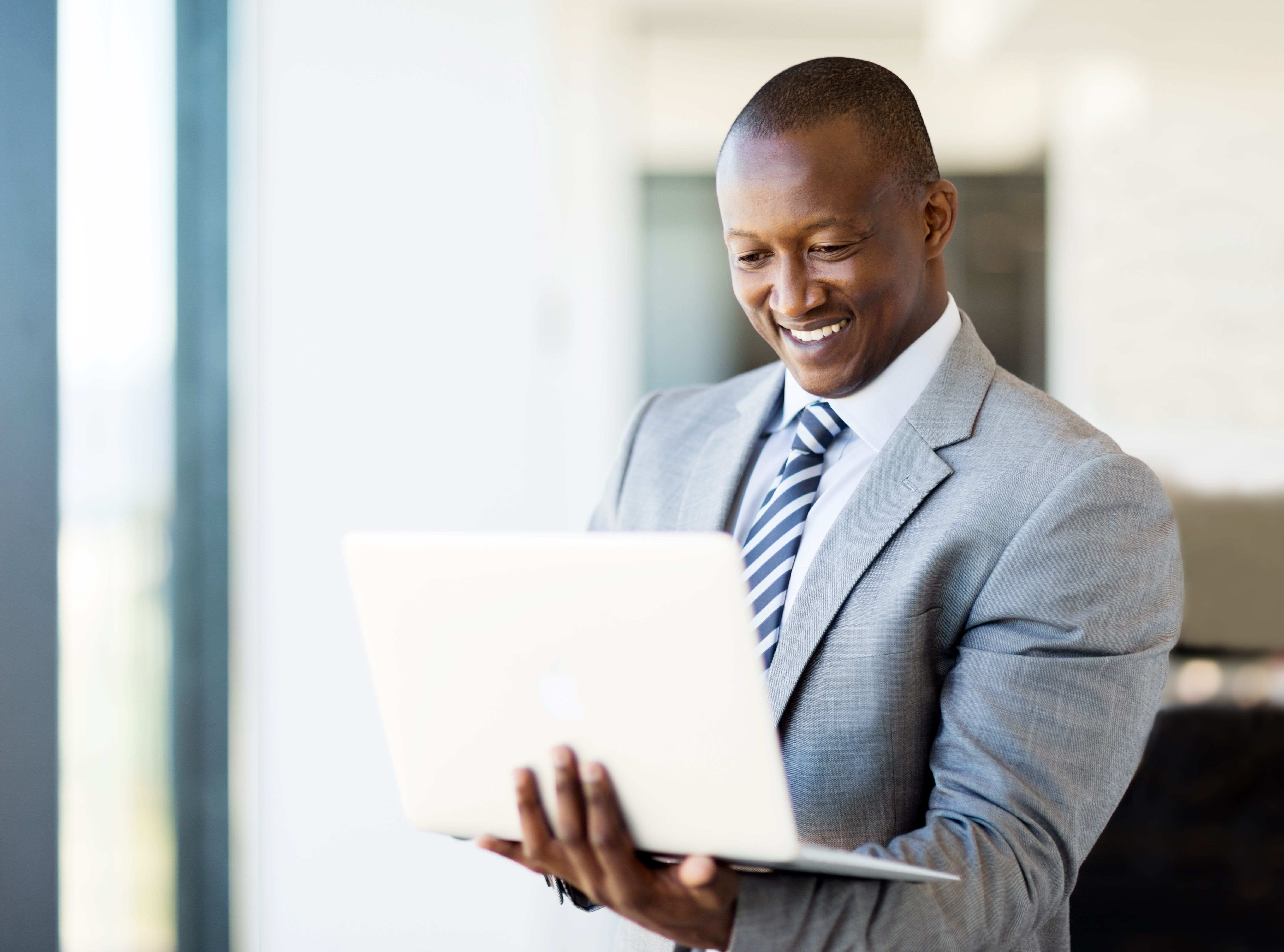 Smiling businessman cradling laptop in left arm while entering content with right hand