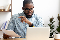 African American businessman sitting behind a laptop looking pleased at his computer screen