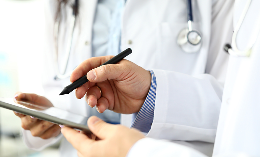 Close up of physician's hands holding a stylist to a writing tablet