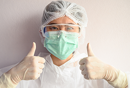 Photo of an Asian woman in hairnet, facemask and latex gloves giving the thumbs up sign with both hands